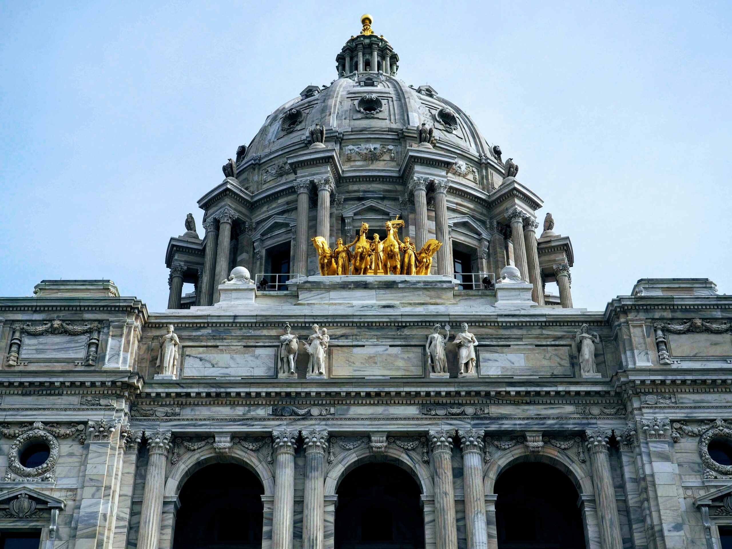 Stone domed cathedral facade with ornate columns and a gold sculpture group atop the balcony.