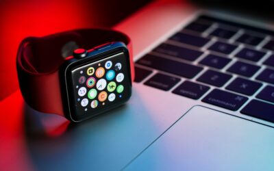 Apple Watch with colorful app icons resting on a laptop keyboard under red and blue lighting