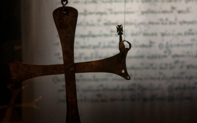 Close-up of a rusted metal scale arm with a hanging bale, against a blurred background of handwritten text.