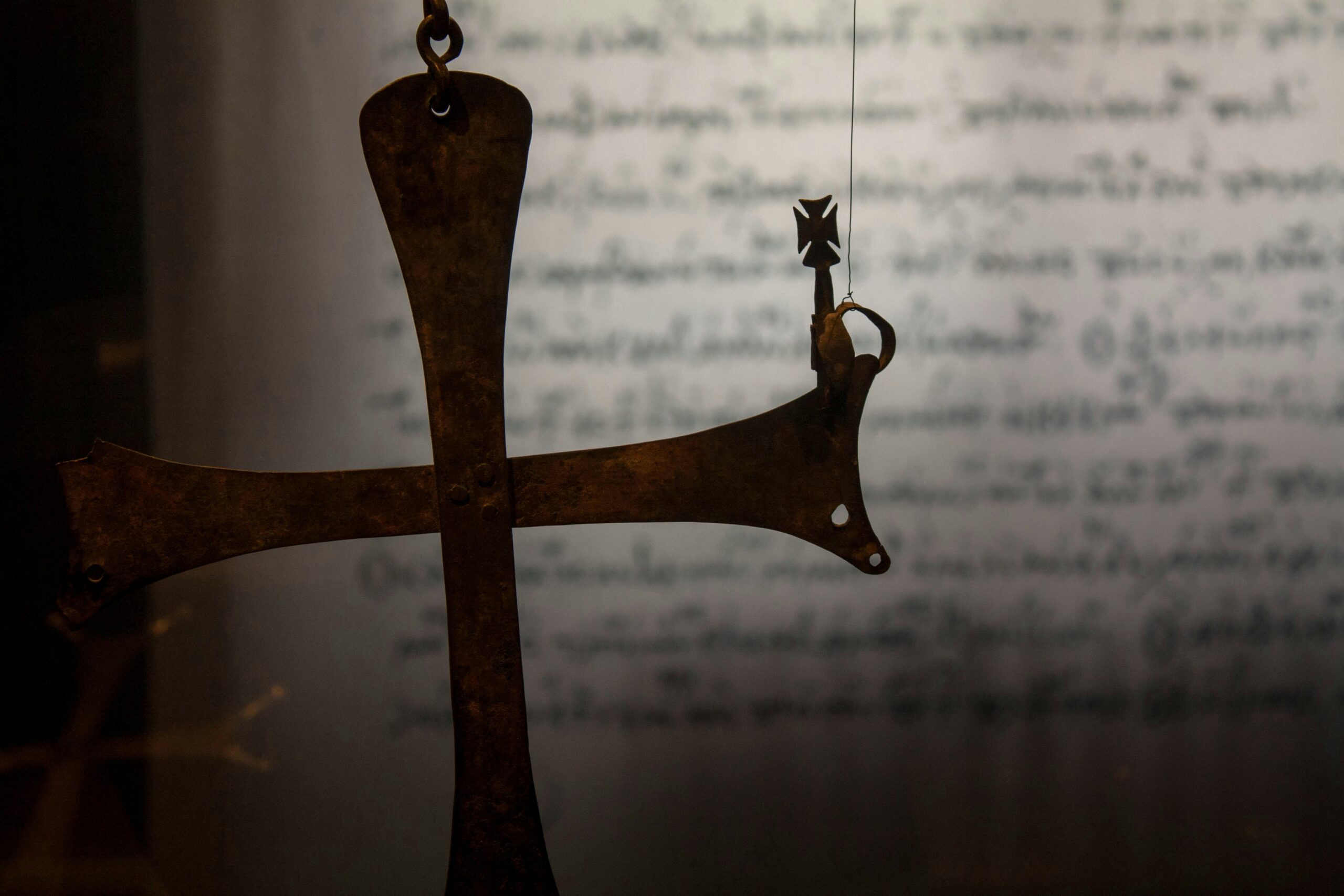 Close-up of a rusted metal scale arm with a hanging bale, against a blurred background of handwritten text.