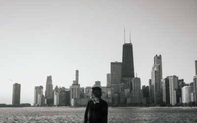 Silhouette of a person by the water with a distant city skyline of tall skyscrapers.