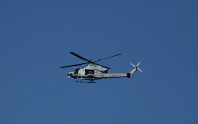 Military helicopter in midflight over a clear blue sky with rotor blades spinning.