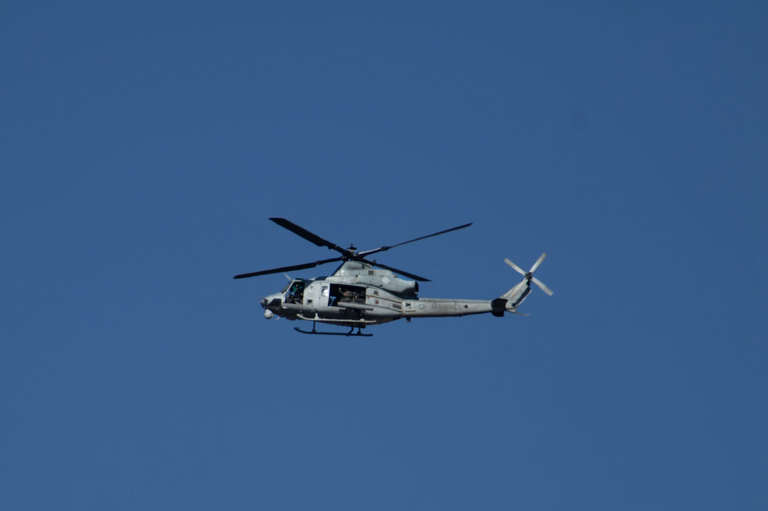 Military helicopter in midflight over a clear blue sky with rotor blades spinning.
