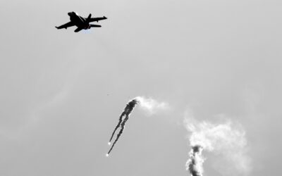 Fighter jet in ascent, leaving curling white smoke trails in a gray sky.