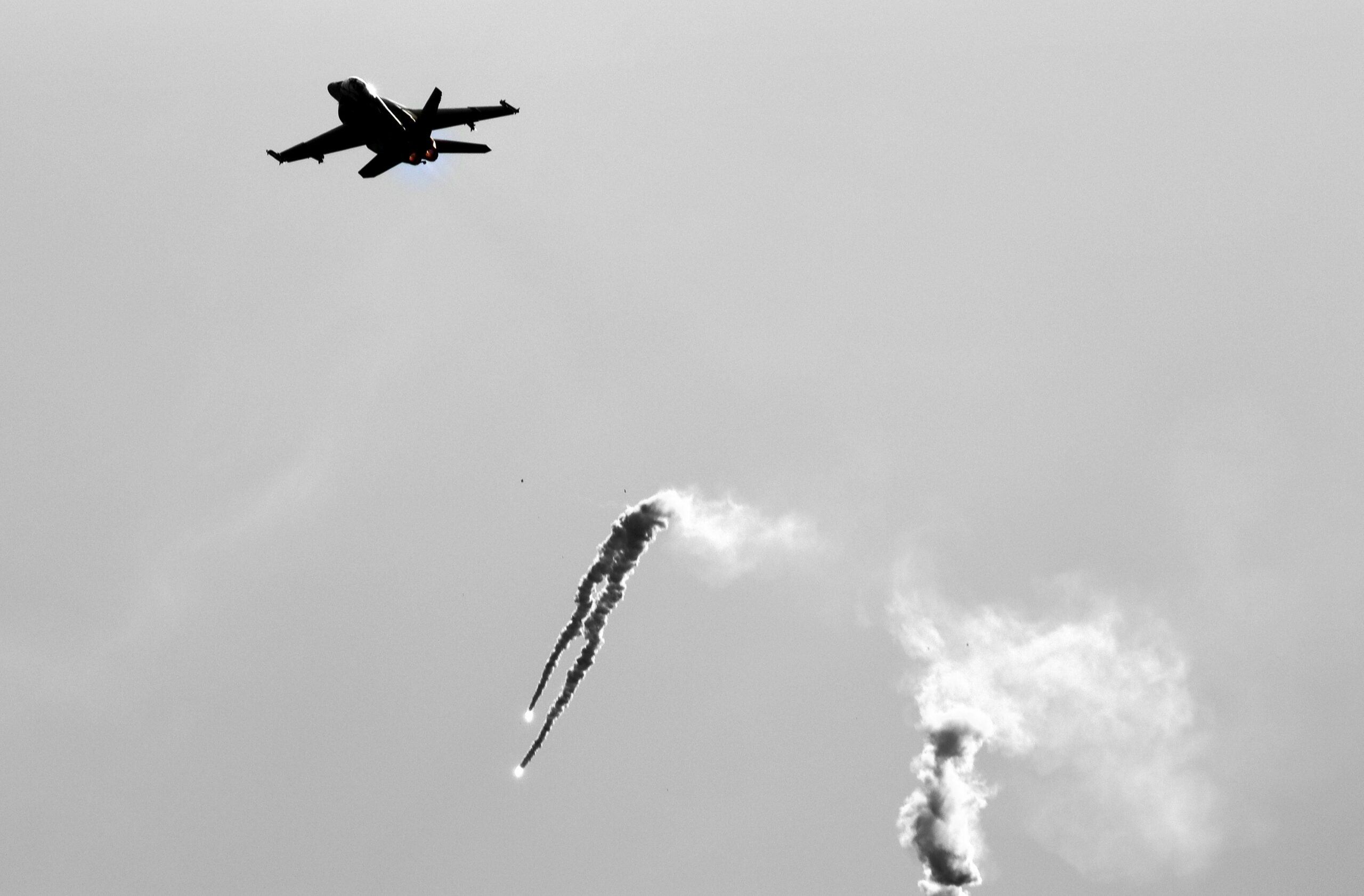 Fighter jet in ascent, leaving curling white smoke trails in a gray sky.