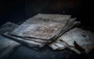 Stack of yellowed, old papers and ledgers spread on a dusty surface in a dimly lit environment.