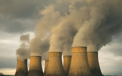 Row of large cooling towers releasing steam into a cloudy sky at an industrial power plant