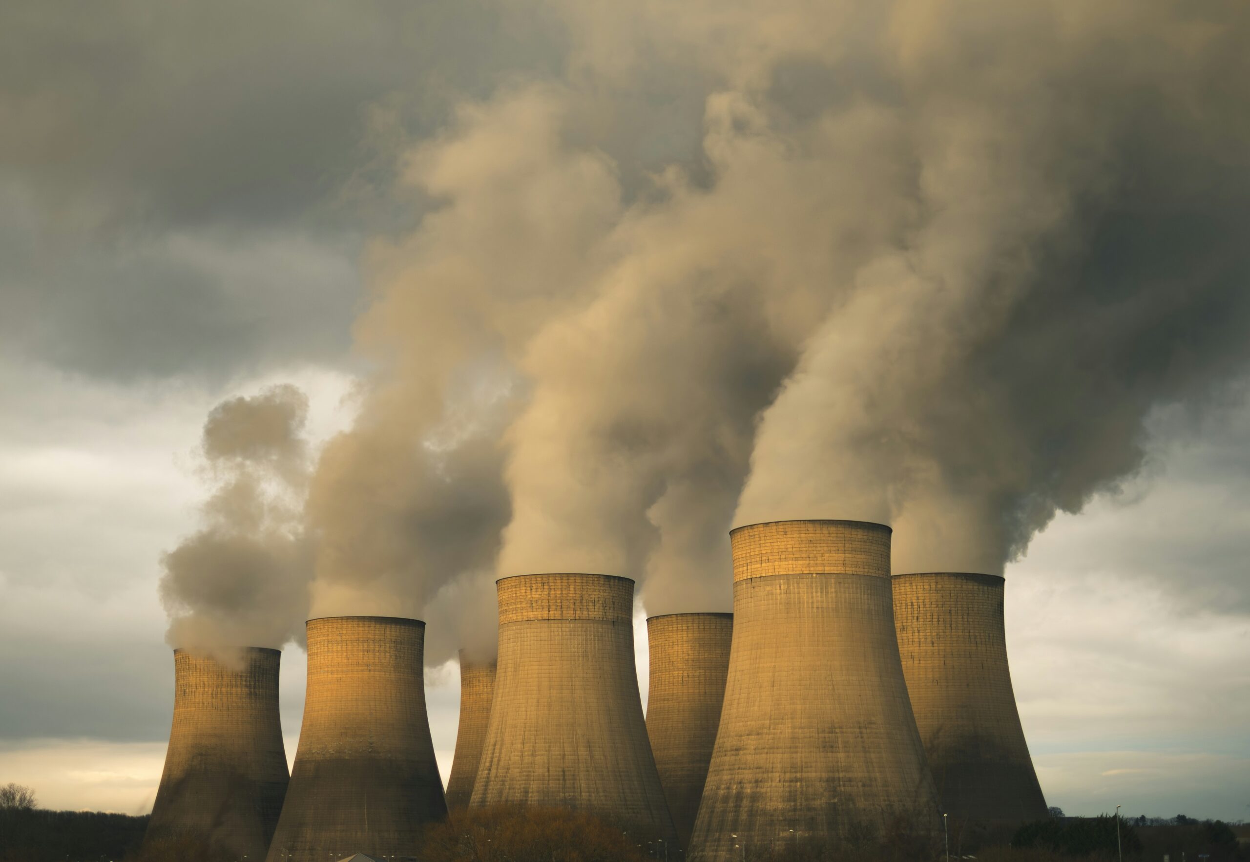 Row of large cooling towers releasing steam into a cloudy sky at an industrial power plant