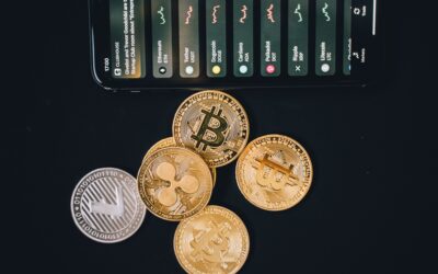 Coins of Bitcoin and other cryptocurrencies on a dark surface with a tilted smartphone displaying a crypto app above them.
