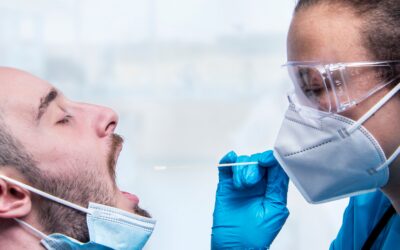 Healthcare worker in goggles and blue gloves swabs a patient’s nose with a cotton swab during a test.