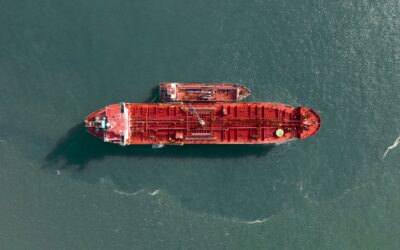 Aerial view of a large red cargo ship sailing on calm teal water. (top-down shot)