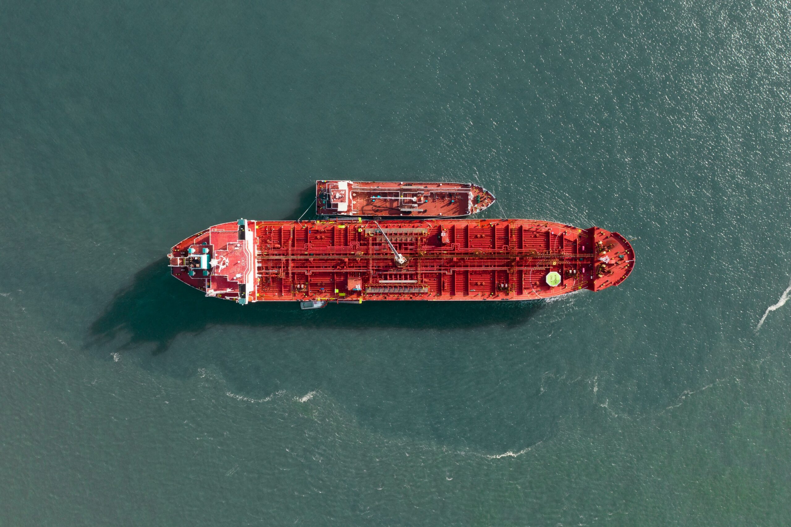 Aerial view of a large red cargo ship sailing on calm teal water. (top-down shot)